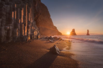 Der schwarze Sandstrand Reynisfjara kurz bevor die Sonne hinter den dramatischen Felsnadeln Reynisdrangar untergeht.