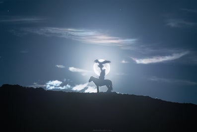 A Mongolian eagle hunter is silhouetted with their bird and horse against a full moon.