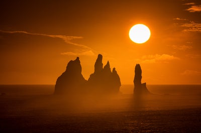 Die Mitternachtssonne erleuchtet die Felsstrukturen direkt vor der Küste am schwarzen Sandstrand von Reynisfjara.