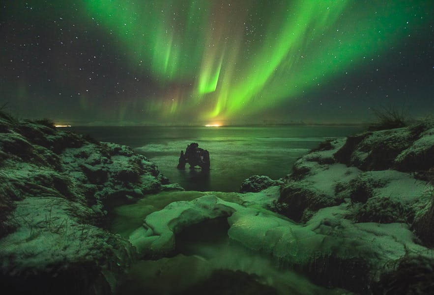 The Aurora flashes in the night skies above the Icelandic coast and rock column - Iceland Photography | Everything You Need To Know