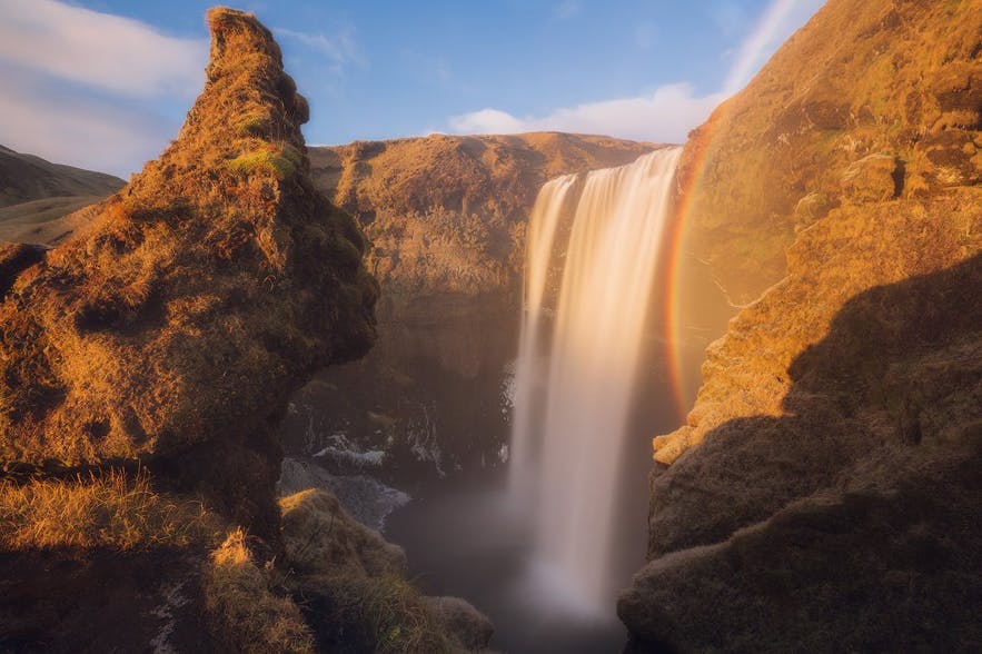 Alt Text: A rainbow appears next to a waterfall - Iceland Photography | Everything You Need To Know