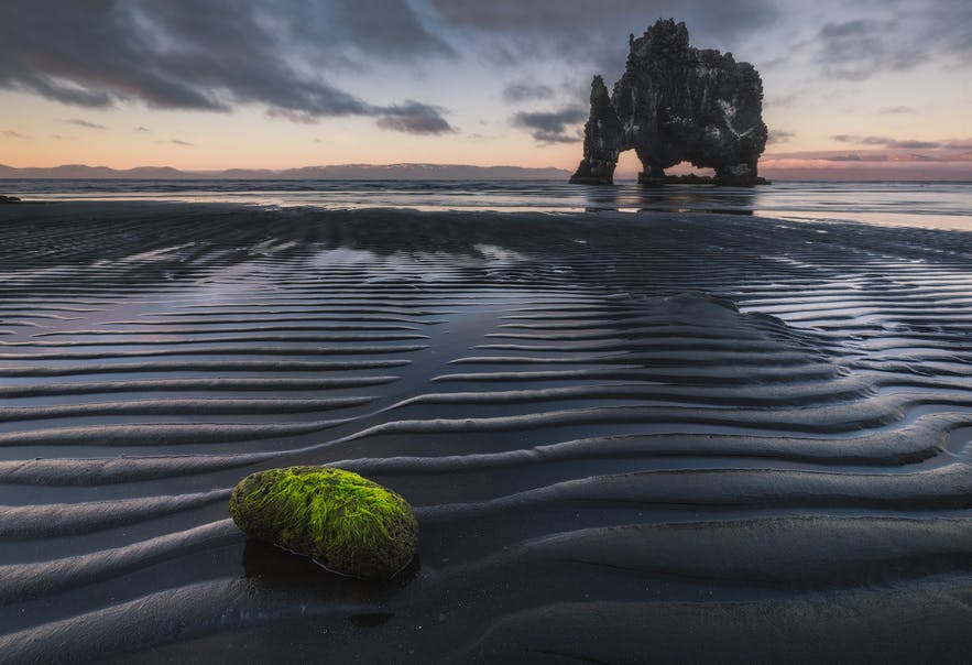 A mossy rock in the foreground leads to a rock formation that sticks out of the sea - Iceland Photography | Everything You Need To Know