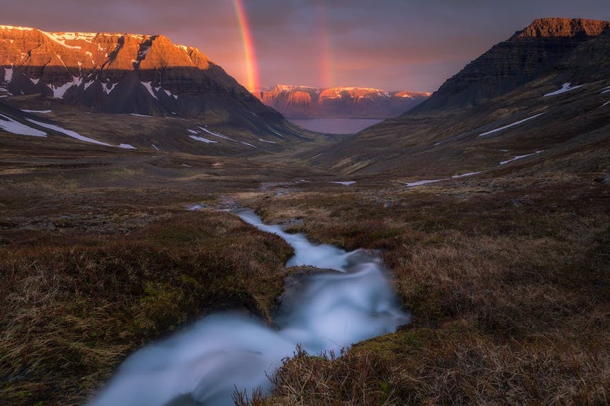 A river winds through the landscape leading to a double rainbow in the background - Iceland Photography | Everything You Need To Know