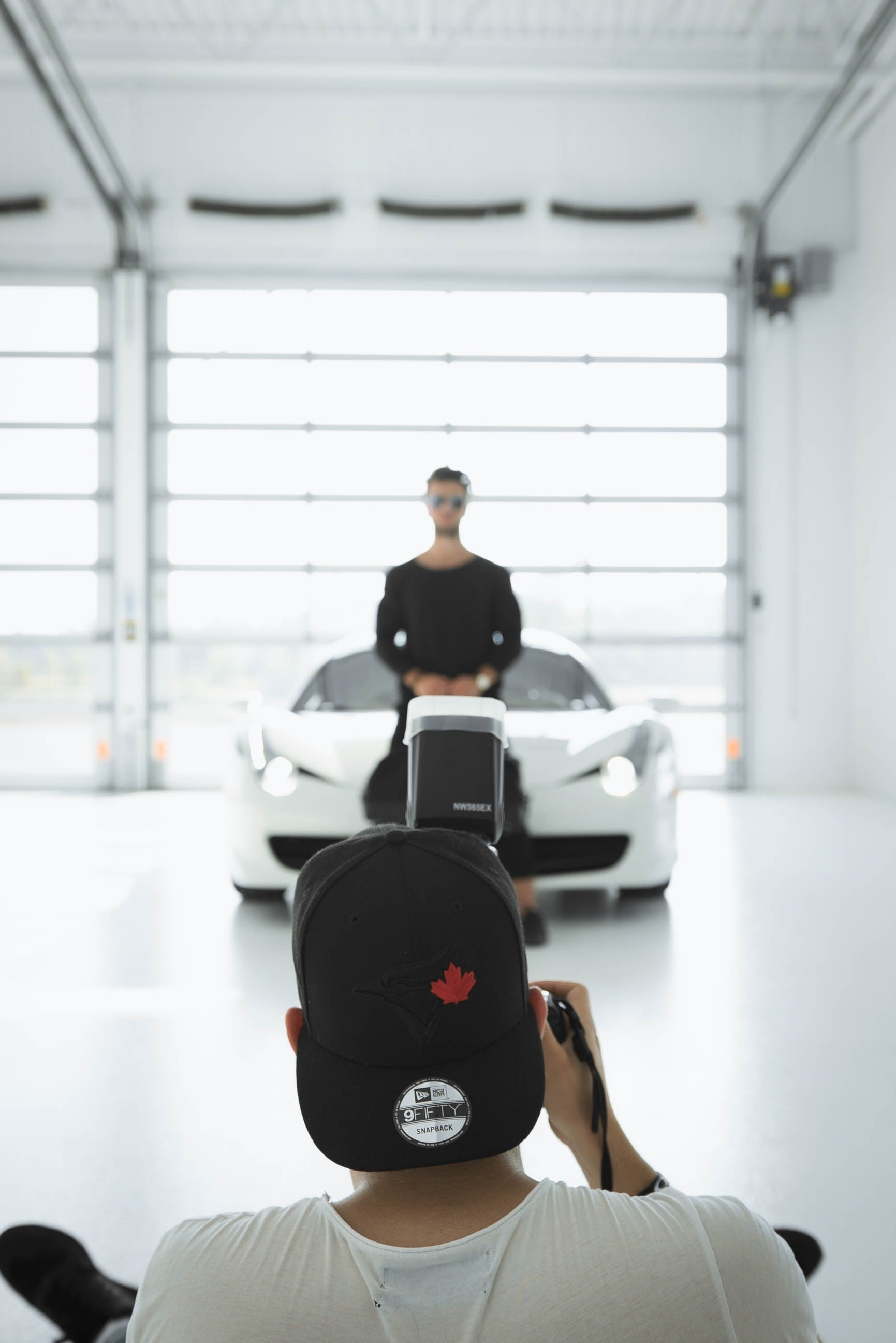 A photographer in a black cap captures a man and white sports car in a studio environment