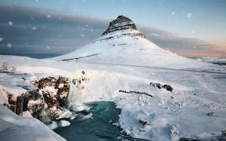 Kirkjufell mountain stands tall and majestic in a serene winter wonderland.