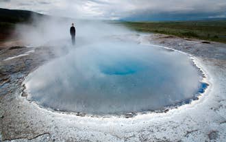 A person stands amid a mystical mist at the Geysir geothermal area on Iceland's Golden Circle driving route.