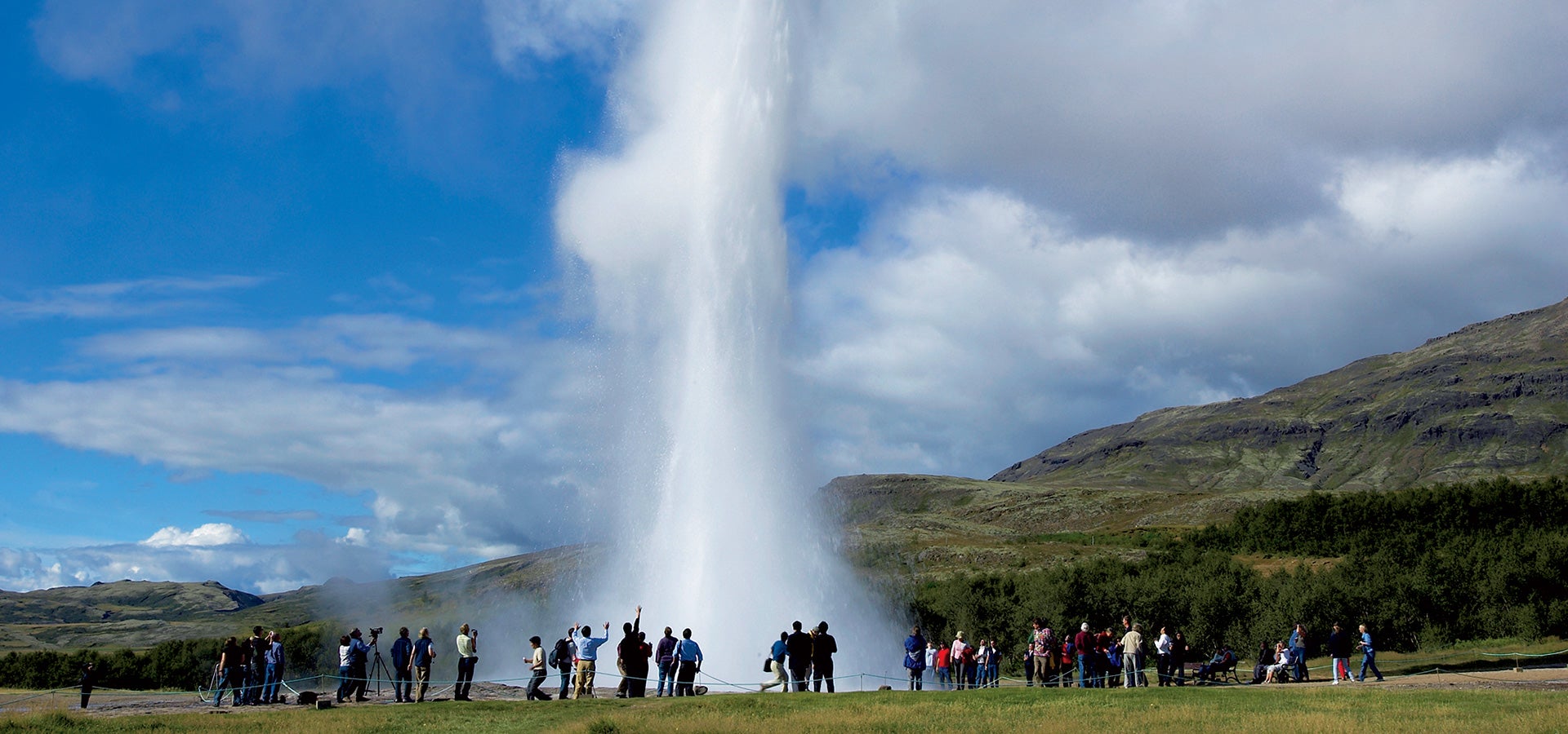 People gather round to watch the Strokkur geyser erupt in the Geysir geothermal area.