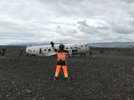 A person in an orange suit pretending to direct air traffic at the DC-3 plane wreck at Solheimasandur beach.