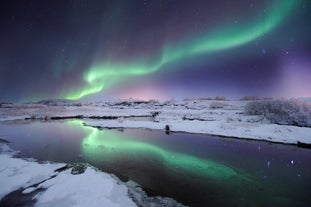 The northern lights produce a dazzling streak of color across the starry winter night sky, that reflects onto the water below.