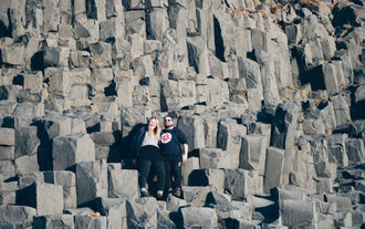 A couple sat on the basalt columns of Reynisfjara black sand beach during a tour in Iceland.