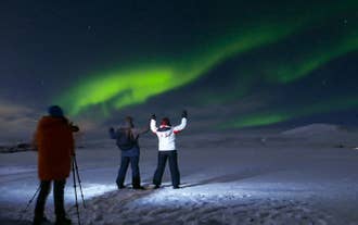 A photographer-guide taking photos of two travelers with the aurora borealis in the background.