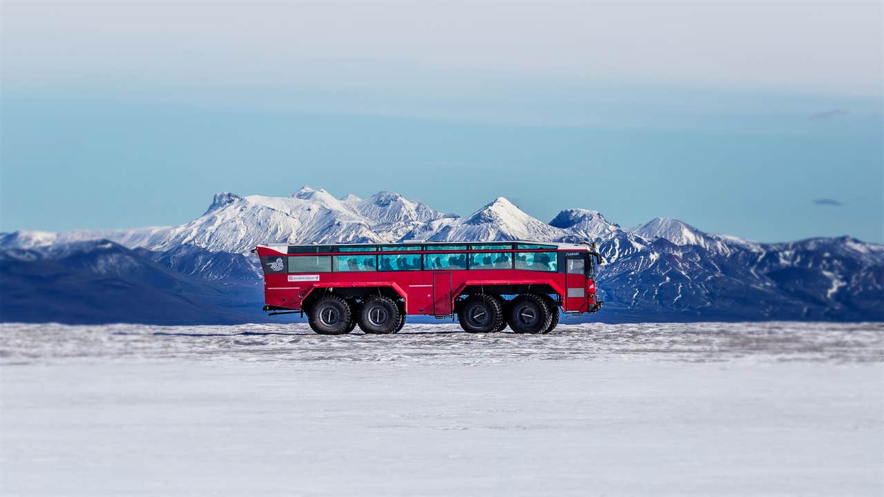 A red monster truck on the Langjokull glacier contrasts perfectly with its white surroundings, including a stunning mountain backdrop.