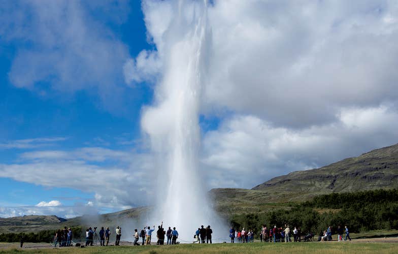 People watch at the Strokkur geyser erupts high into the air at the Geysir geothermal area on Iceland's Golden Circle driving route.