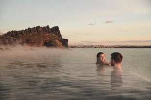 People relax at the Sky Lagoon pool's infinity edge, with a distant view of Reykjavik behind.