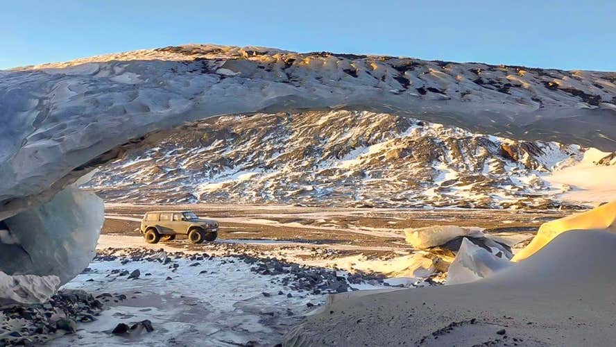 A super jeep easily traverses Iceland's rugged terrain, surrounded by splatters of snow across the landscape.