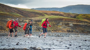 Hikers on the Laugavegur hiking trail in the Icelandic Highlands wade through a shallow river.