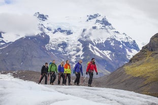 People walk in a line along the Falljokull glacier during a guided tour, with breathtaking mountain scenery behind them.