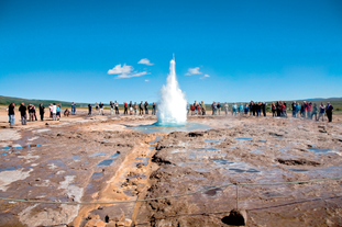 People stand near the Stokkur geyser as it erupts high into the air at the Geysir geothermal area on Iceland's Golden Circle sightseeing route.