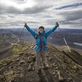 A happy hiker stands with their arms in the air, holding up their hiking poles, on a mountain in the Icelandic Highlands.