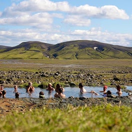 Hikers soak in a natural geothermal pool in a remote area of the Highlands, surrounded by gorgeous scenery.