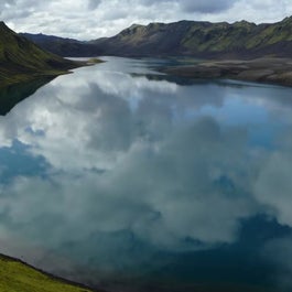 A serene lake in the Icelandic Highlands reflects cloudy skies onto its tranquil waters.