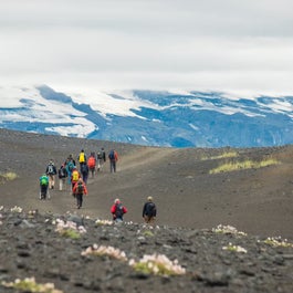 Hikers on the Laugavegur trail walk amid a desolate landscape with stunning, contrasting mountain views ahead.